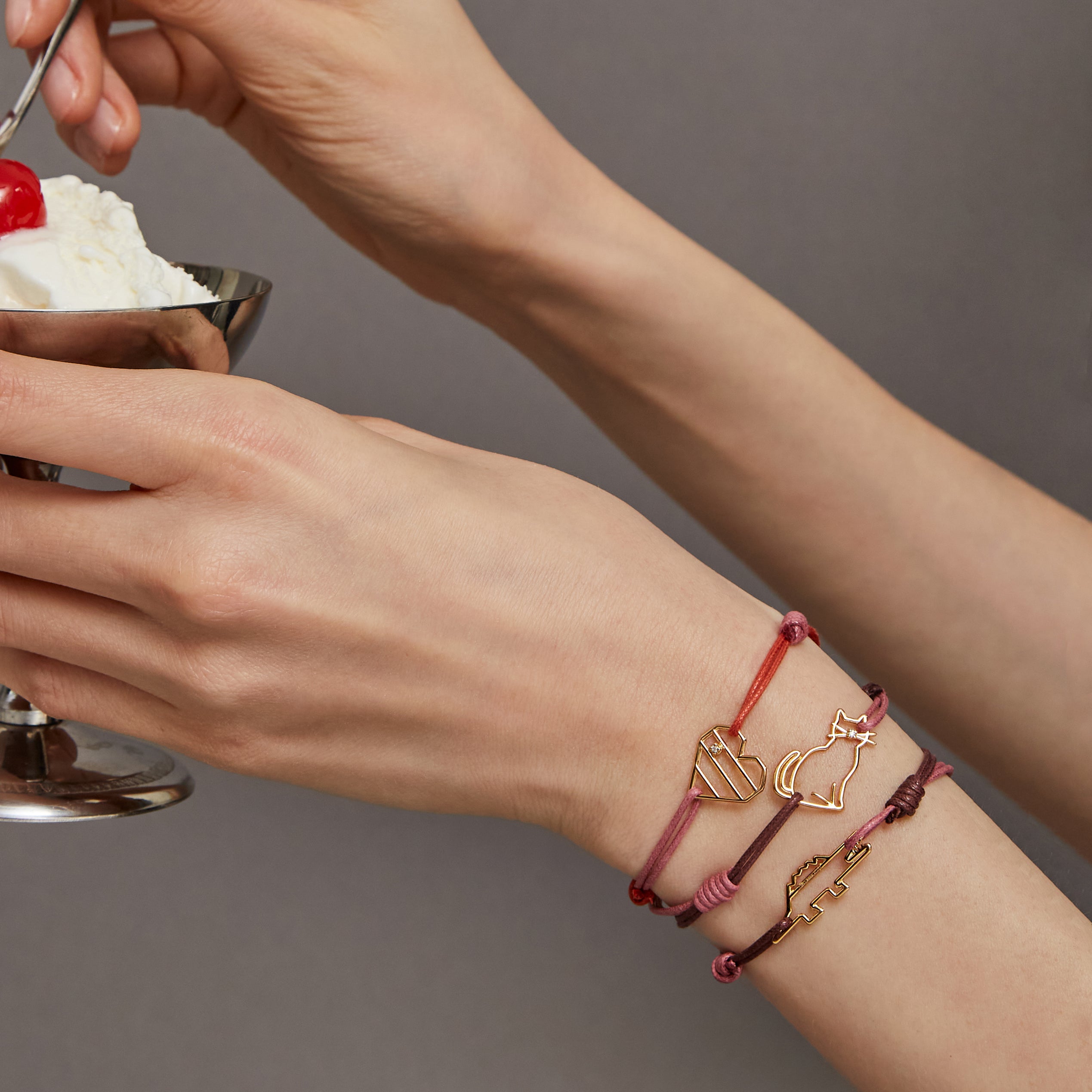 Hands holding an ice cream cup wearing cord bracelets with gold pendants