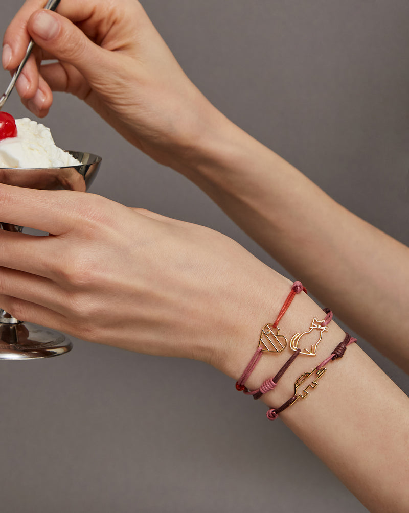 Hands holding an ice cream cup wearing cord bracelets with gold pendants