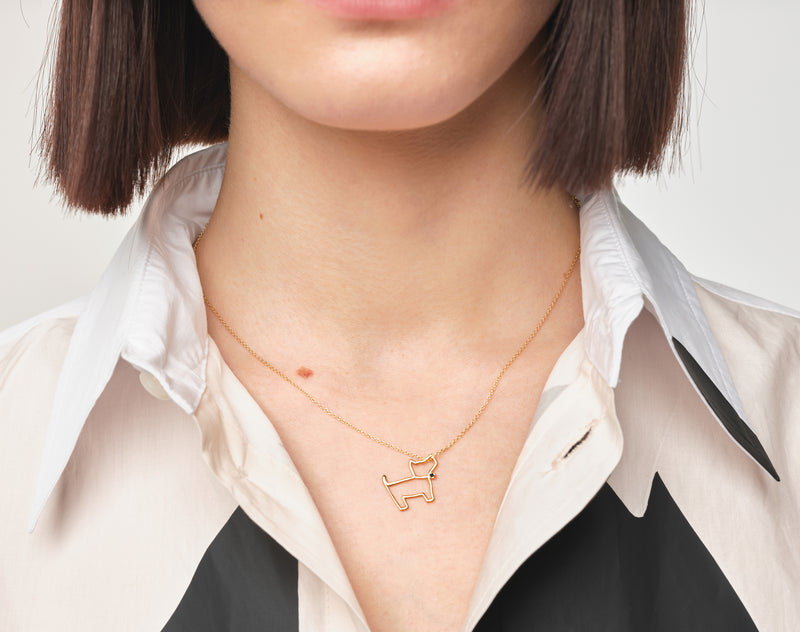 Woman wearing a gold chain necklace with a little dog shaped pendant with a blue sapphire