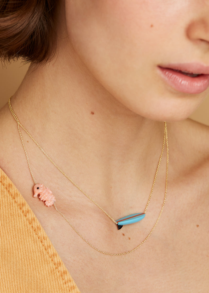 Gold chain necklace wih surf shaped turquoise pendant worn by model
