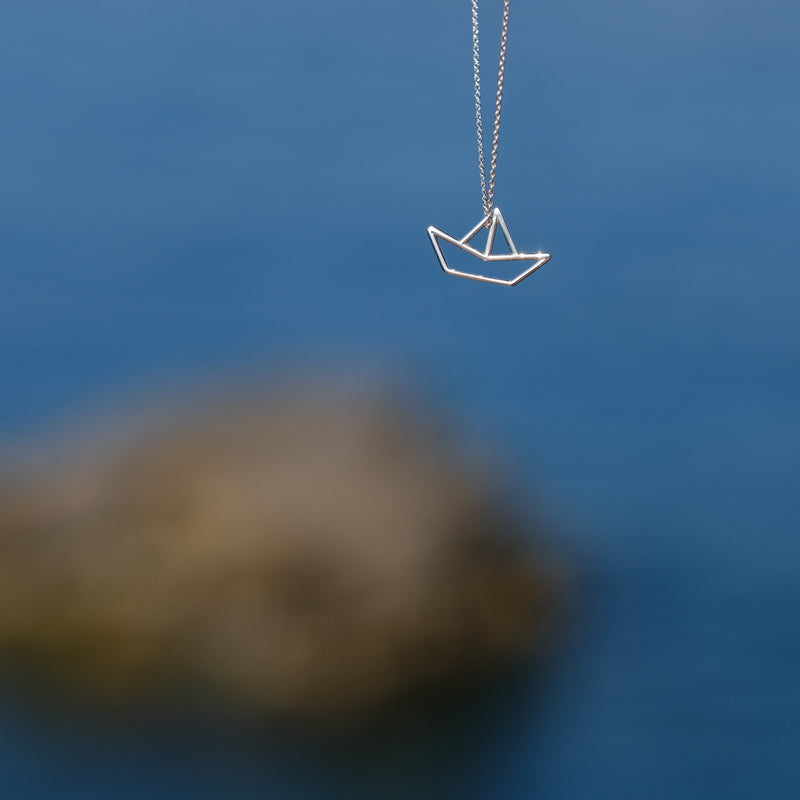 White gold chain necklace with little boat shaped pendant on seaside background
