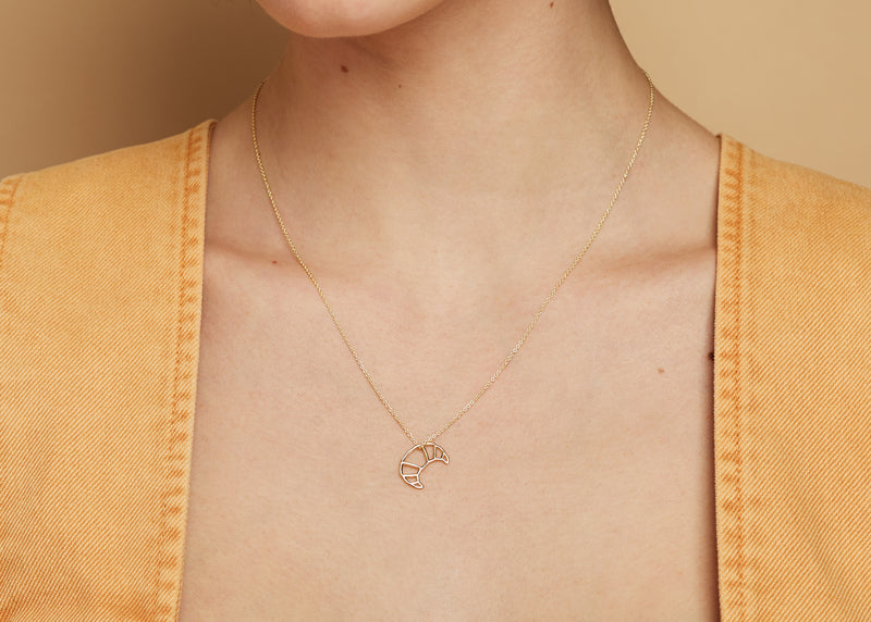 Gold chain necklace with small croissant shaped pendant worn by model