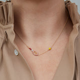 Gold chain necklace with gold tennis racquet and ball shaped pendants in pink and yellow enamel worn by model