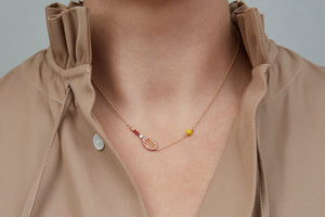 Gold chain necklace with gold tennis racquet and ball shaped pendants in pink and yellow enamel worn by model