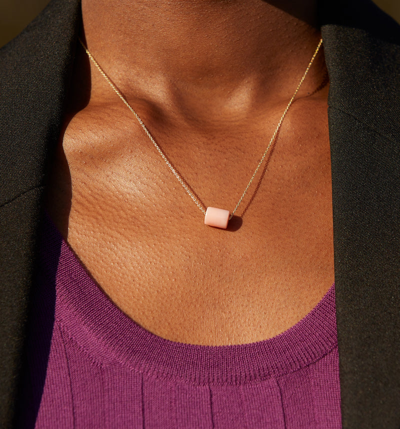 Woman wearing a gold chain necklace with a cylinder pink opal stone