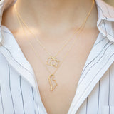 Model wearing gold chain necklaces with small camera and dinosaur pendants with emerald