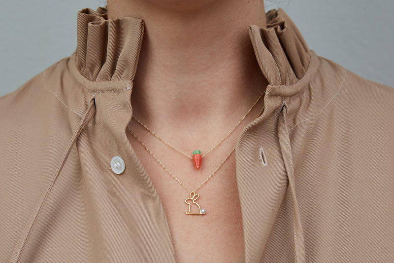 Model wearing gold chain necklaces with carrot shaped coral pendants and rabbit shaped pendant with pearl