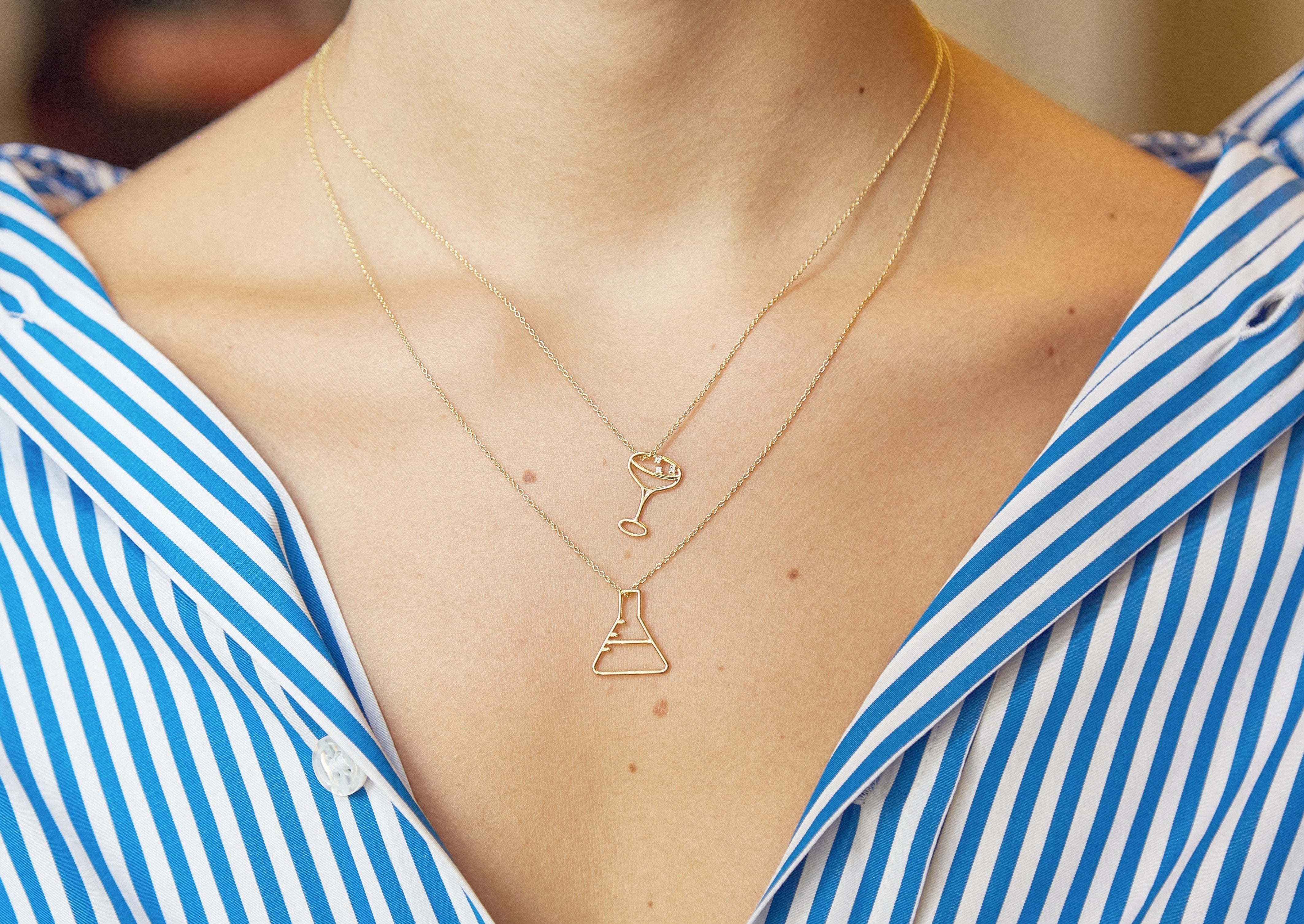 Gold chain necklace with chemistry baker shaped pendant worn by model