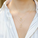 Gold chain necklaces with house and light bulb shaped pendants and small diamond worn by model