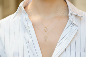 Gold chain necklaces with house and light bulb shaped pendants and small diamond worn by model