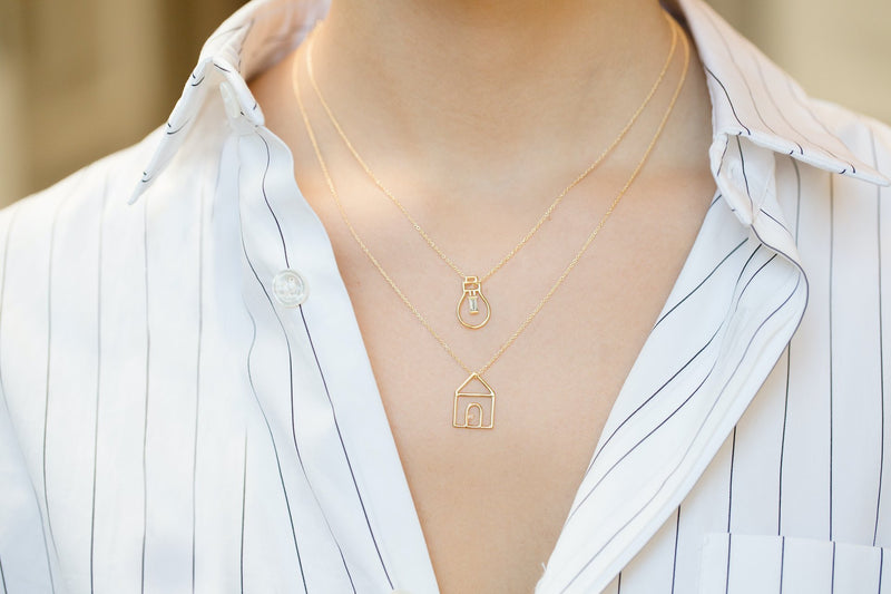Gold chain necklaces with house and light bulb shaped pendants and small diamond worn by model