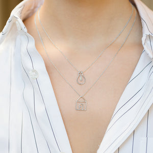 White gold chain necklace with house shaped pendant and small diamond worn by model