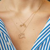 Woman wearing gold chain necklaces with small camera and rainbow shaped pendants with little stones
