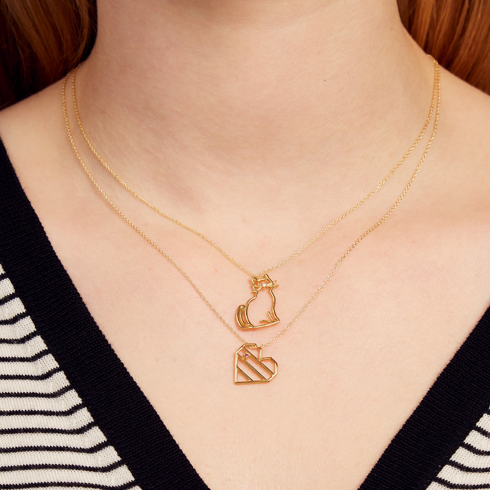 Woman wearing gold chain necklace with a cat shaped pendant with a diamond nose and heart shaped pendant with pink sapphire