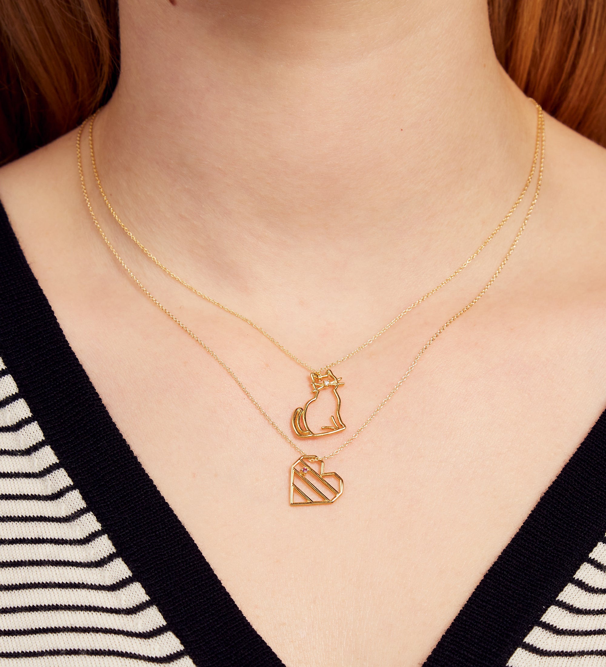 Woman wearing gold chain necklace with a cat shaped pendant with a diamond nose and heart shaped pendant with pink sapphire