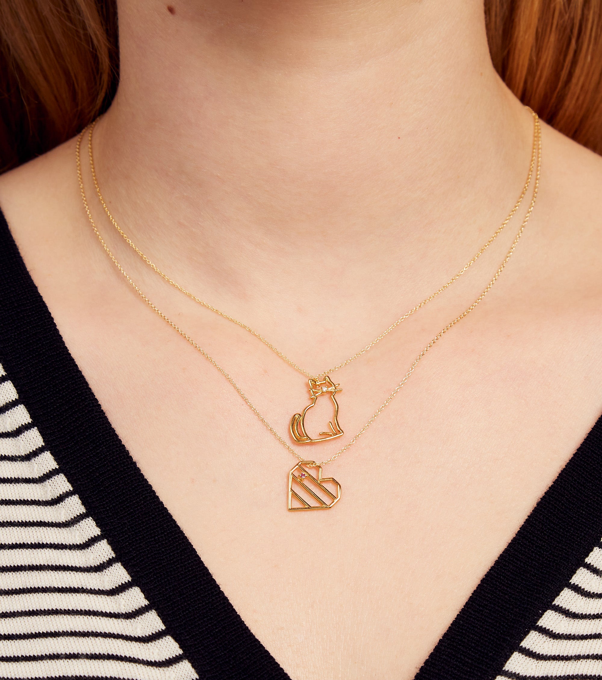 Woman wearing gold chain necklace with a cat shaped pendant with a diamond nose and heart shaped pendant with pink sapphire