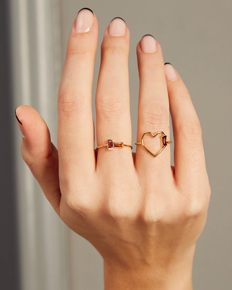 Hand wearing a heart shaped ring with a garnet baguette and a gold ring with baguette cut citrine and pink tourmaline