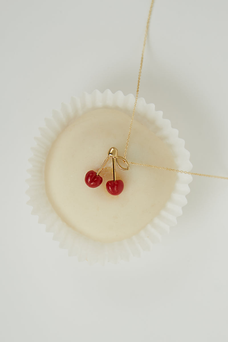 Creamy white pastry with a necklace with coral cherries as pendant on top
