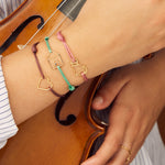 Pink cord bracelet with gold seated cat shaped pendant worn by model holding violin
