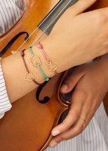 Load image into Gallery viewer, Pink cord bracelet with gold seated cat shaped pendant worn by model holding violin
