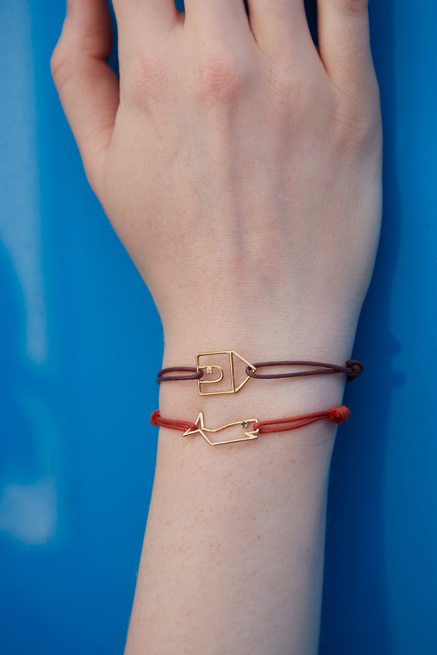 Cord bracelets with a house and whale shaped gold pendants with diamond and blue sapphire