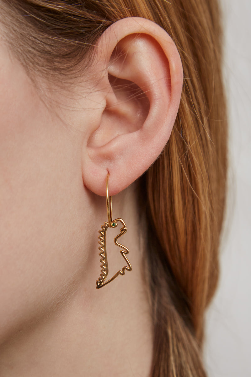 Woman wearing a gold hoop earring with a dinosaur shaped pendant with a small emerald