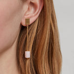 Woman wearing a gold long earring with cylinder cut pink opal
