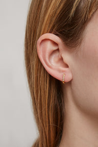 Woman wearing a gold mini hoop earring with a zig-zag finish