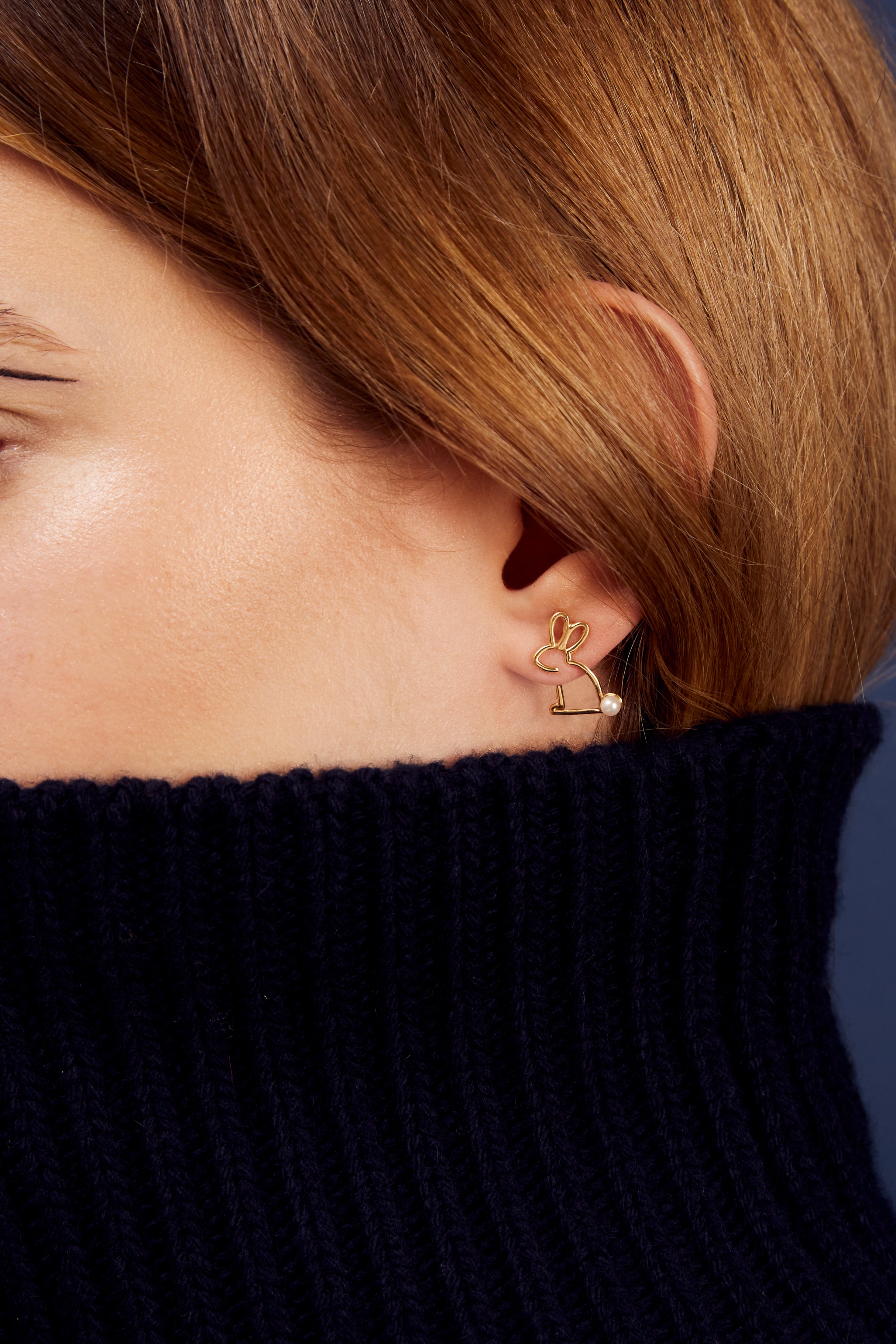 Woman wearing a small rabbit shaped gold earring with a pearl tail