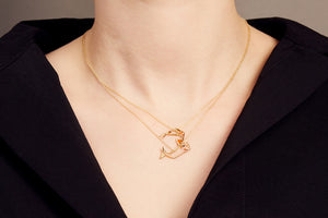 Woman wearing two gold necklaces with shrimp and whale shaped pendants with ruby and blue sapphire