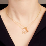 Woman wearing two gold necklaces with shrimp and whale shaped pendants with blue sapphire