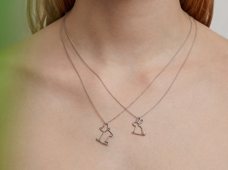 Woman wearing two white gold chain necklaces with a dog and rabbit shaped pendants
